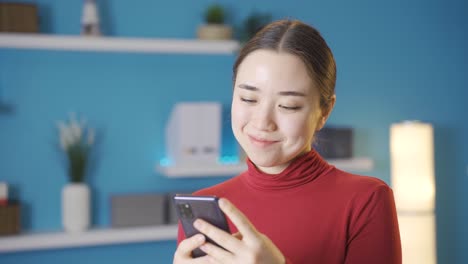 아시아 여성이 집에서 행복하게 전화를 보고 있습니다.