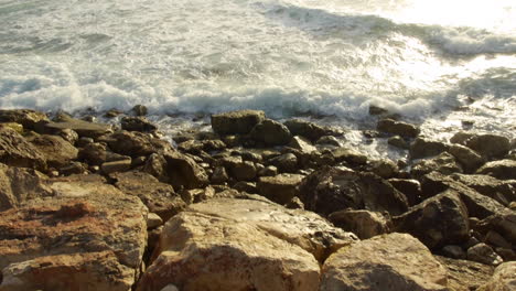 olas rompiendo en las rocas en la orilla, brillante sol vespertino