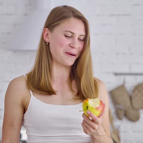 fit smiling young woman eating healthy fruit. beautiful girl enjoys eating fresh sweet apple on the modern kitchen background. concept of losing weight.