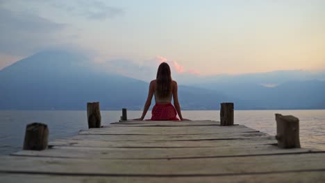 girl sitting on pier watching the sunset over a volcano in lake atitlan, guatemala