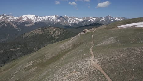 aerial follows barren ridge trail to man on rocky mountain viewpoint