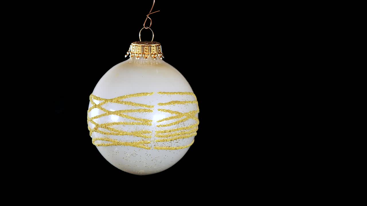 single white Christmas ball ornament with golden glitter stripes and black background, close up