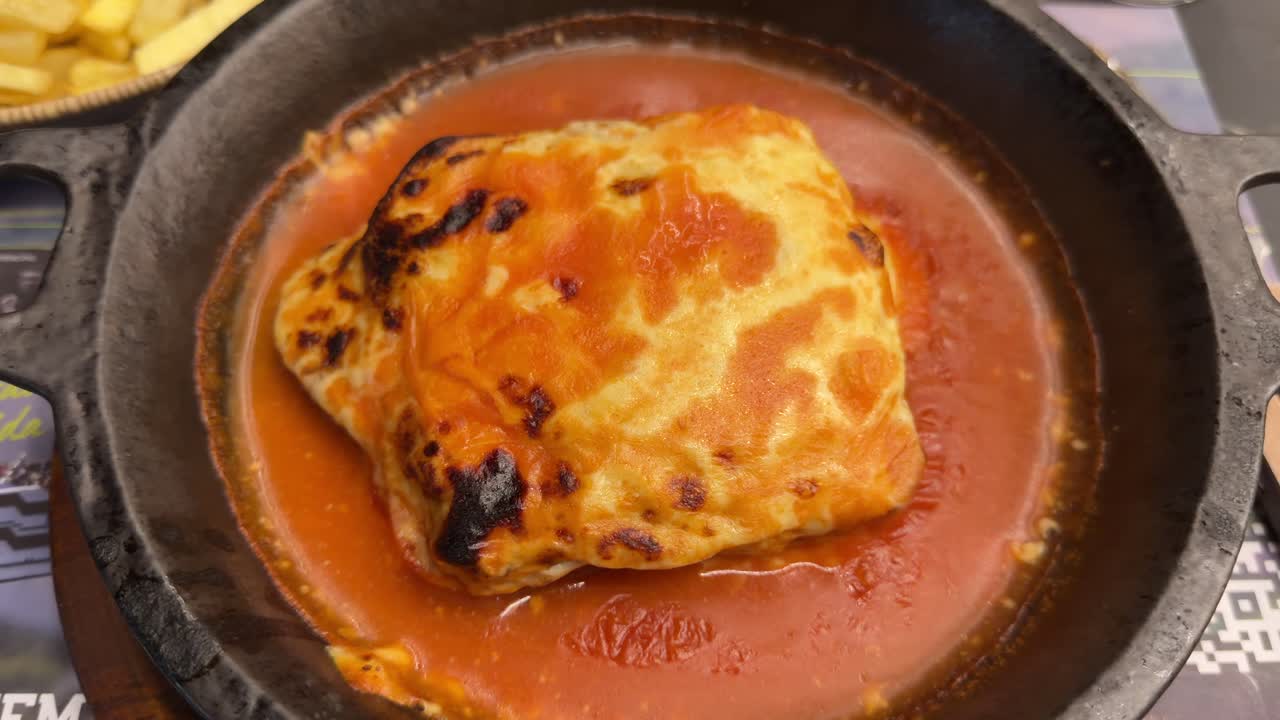Francesinha coperta di salsa servita in un piatto di ceramica.