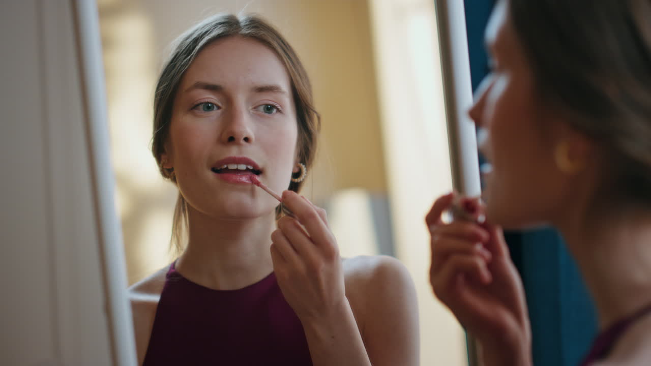 Woman applying shiny lipstick in mirror reflection closeup. Attractive girl do