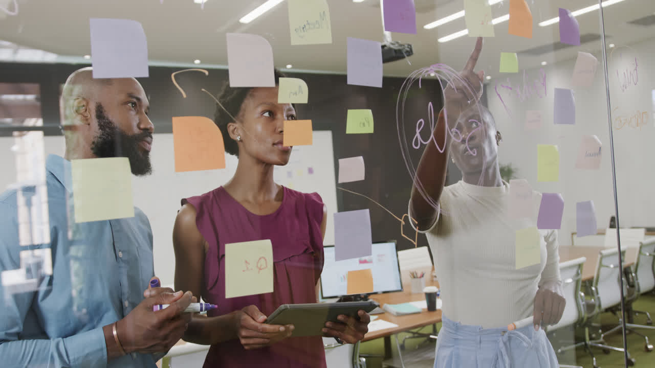 African american colleagues brainstorming, making notes on glass wall in office in slow motion