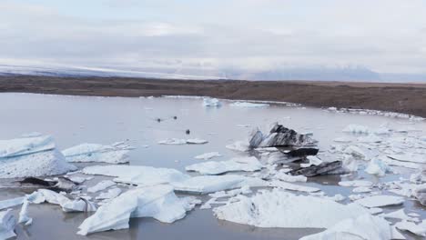 tourist in three small boats visiting icebergs floating in glacial lagoon, aerial