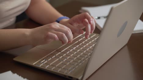 las manos femeninas están escribiendo texto en el teclado de la computadora portátil. los dedos presionan rápidamente las teclas del teclado. hay un cuaderno al lado. computadora personal, trabajo remoto en casa, negocios, estudio, mensajería, chat