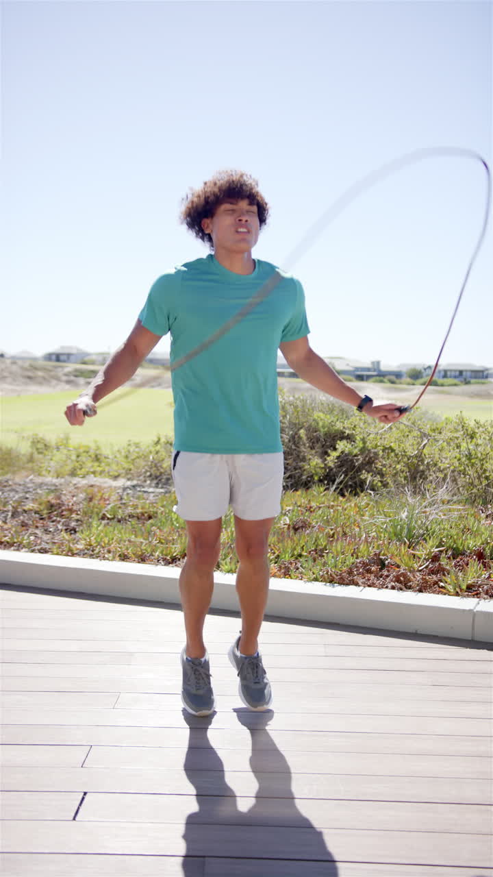 Vertical video: A young biracial man skipping rope, blue sky background