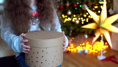 portrait of happy little girl sitting near christmas tree on new year's eve in decorated room. new year and holidays with kids concept. enjoying festive holiday celebration.