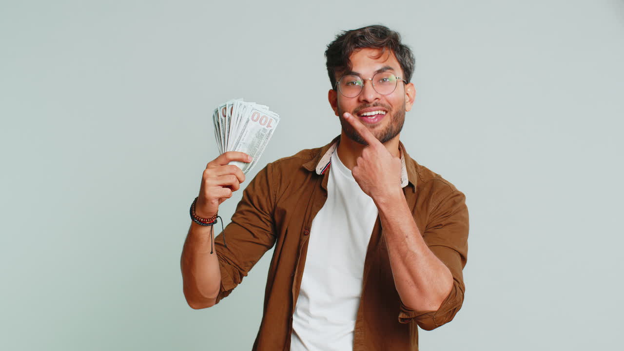 Rich happy Indian man winner waving money dollar cash like a fan, big income wealth success business