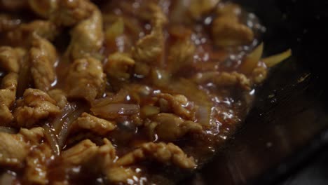 onions and chicken fry on high heat in chinese metal wok pan, close-up