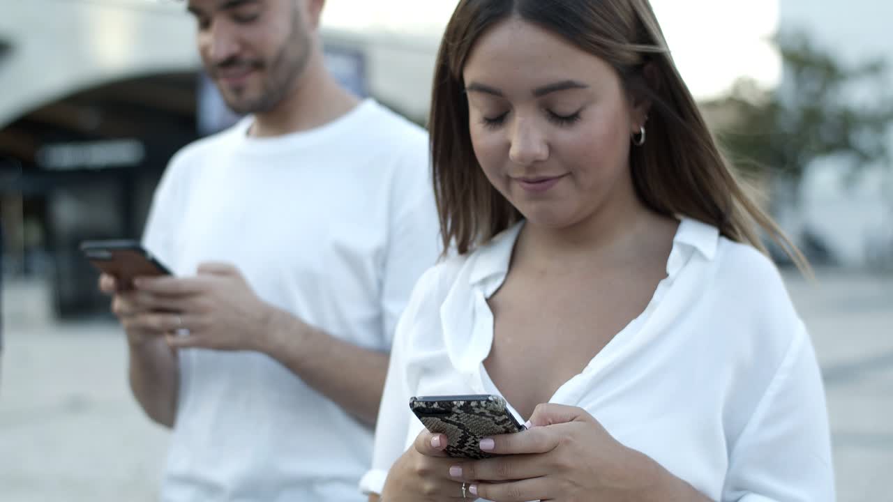 mujer caucásica sonriente caminando por la calle con un teléfono inteligente