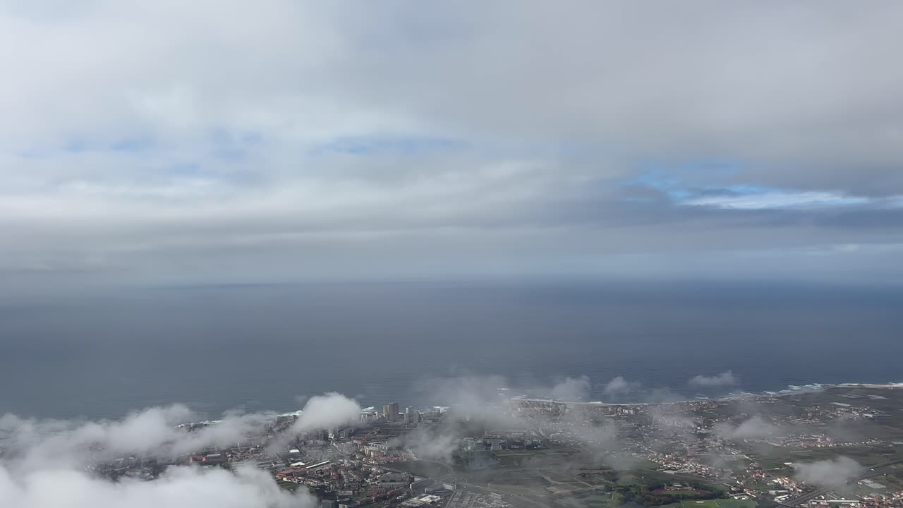 Panoramic airplane view of coastal landscape and sea beneath layered clouds