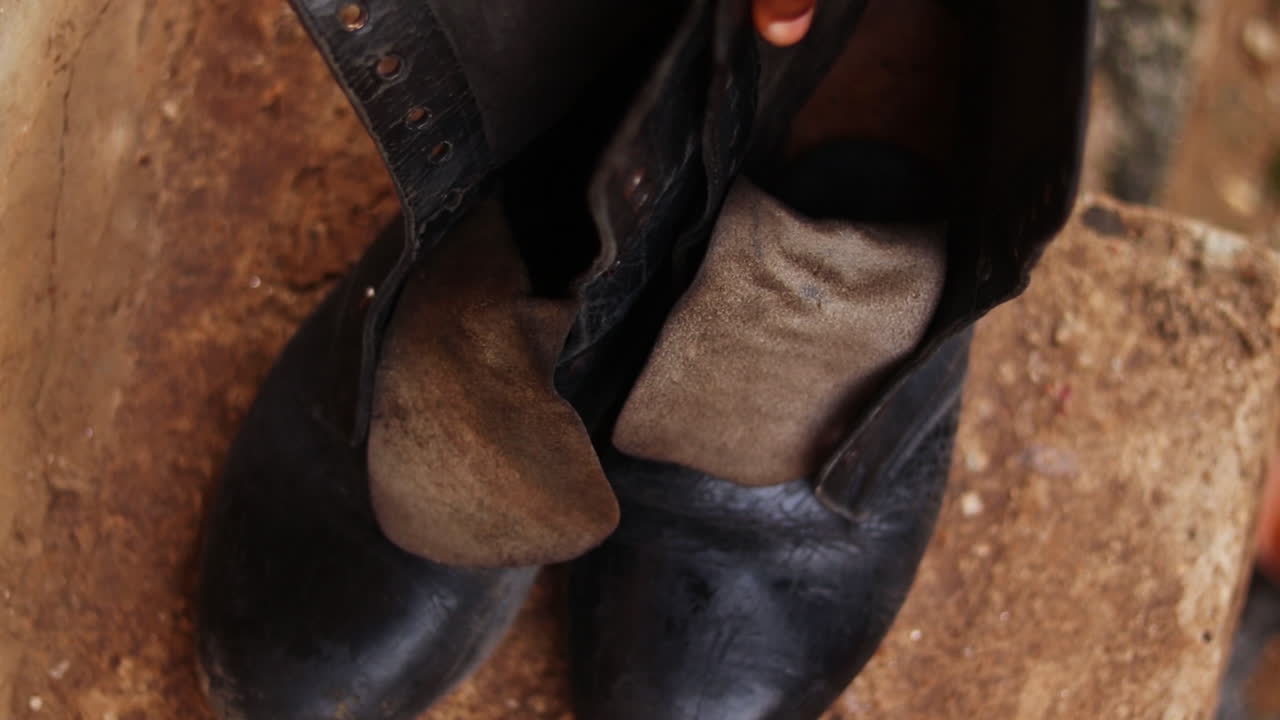 Hand placing worn black boots on a curb