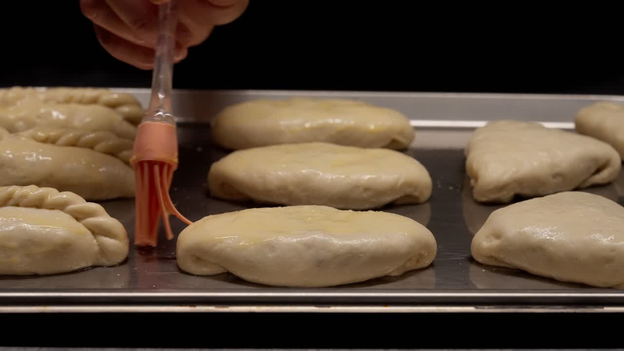 Hand Brushing Egg Wash on Unbaked Pastries on a Baking Tray