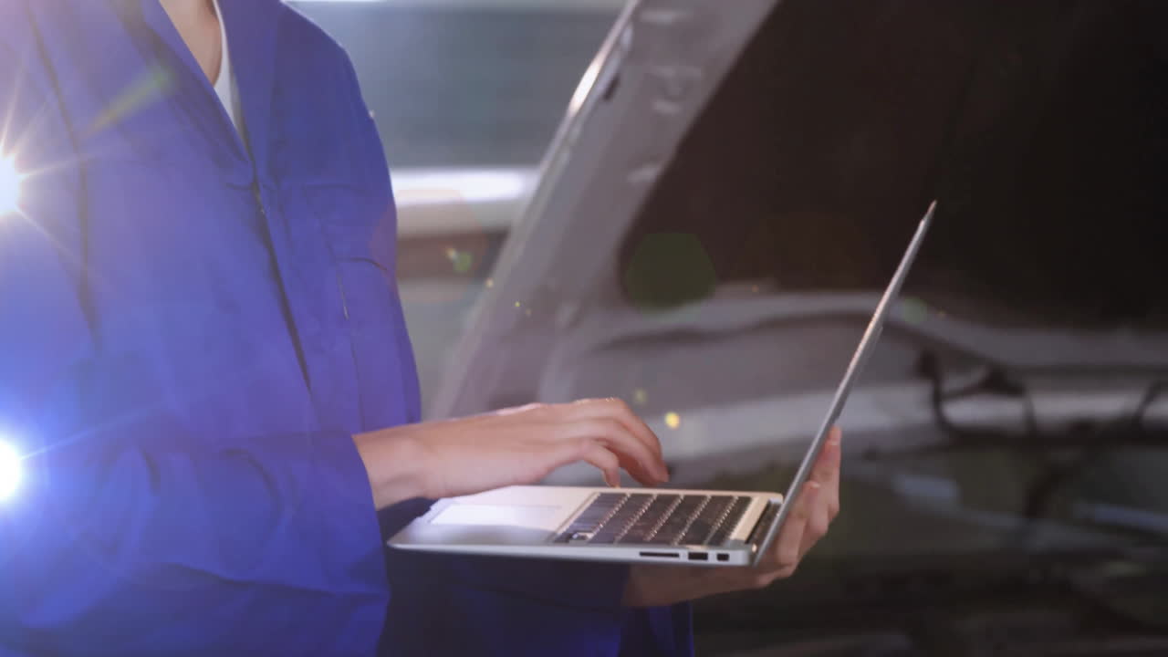 female mechanic typing on laptop in automotive workshop, with animated data graphs over engine bay