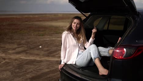 portrait of a woman traveler having a break sitting in car trunk barefoot, relaxing