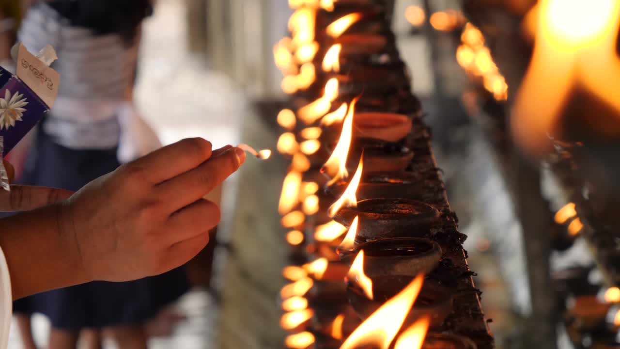 Closeup 4k video of worshipper lighting up the wick of sacred oil lamp at buddhist temple