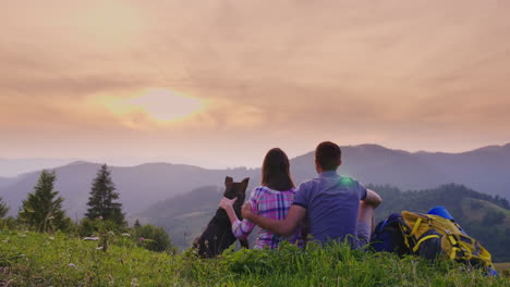 Ein-Paar-Touristen-Mit-Hund-Bewundern-Die-Schöne-Landschaft-In-Den-Bergen-Sie-Sitzen-Auf-Dem-Boden