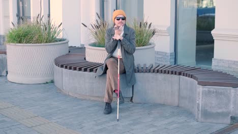 visually impaired man talking on the phone, sitting on the bench in the city.