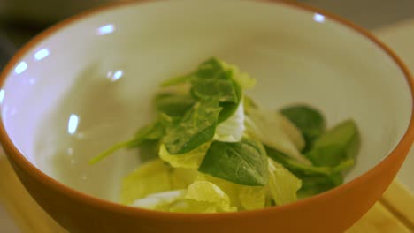 the cook puts fresh green spinach leaves and napa cabbage in to the white clay pot, making pasta salad, handheld close up shot