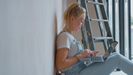 Eine-Frau,-Die-Zu-Hause-Ein-Zimmer-Renoviert,-Sitzt-Mit-Einem-Laptop-Auf-Dem-Boden-Und-Macht-Eine-Pause-Vom-Dekorieren