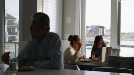 Vista-Frontal-De-Una-Familia-Asiática-Multigeneracional-Comiendo-Comida-En-La-Mesa-Del-Comedor-En-Una-Casa-Cómoda-4k