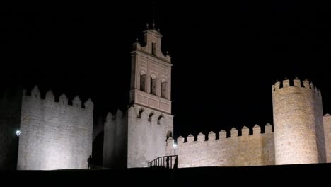 silhouette of people against avila’s medieval walls, illuminated at night with the historic old town in the background, a unesco site in spain.
