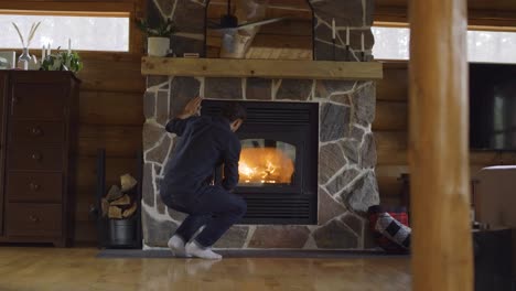 a man tends a fire in a stone fireplace inside a cozy log cabin