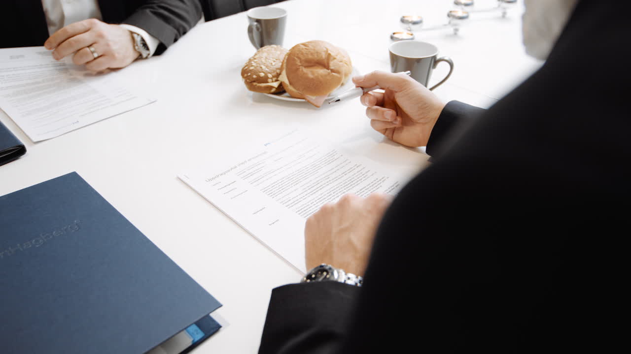 Two people in suits in business meeting looking reviewing agreement signing contract with signature buying bank bonds financial banking important papers coworkers deal realtor real estate purchase job