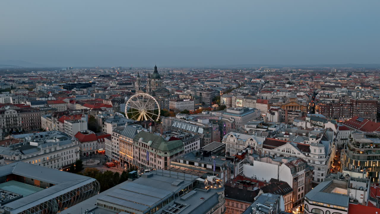 Evening settles over central Budapest as the Ferris wheel and St. Stephen’s Basilica rise amid vibrant streets and classic rooftops