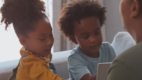 Nahaufnahme-Einer-Mutter-Zu-Hause-Im-Wohnzimmer-Mit-Kindern,-Die-Gemeinsam-Auf-Dem-Sofa-Ein-Buch-Lesen