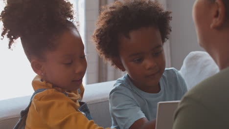 close up of mother at home in lounge with children reading book on sofa together
