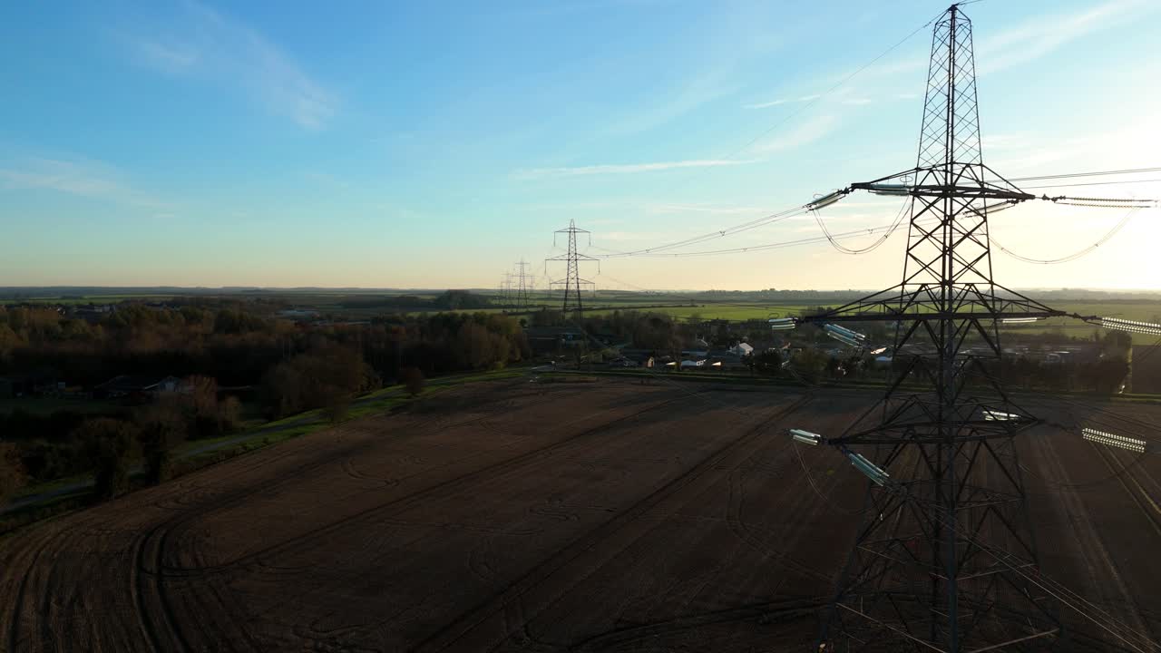 Aerial drone view of a high voltage electrical pylon silhouetted against a vibrant golden hour sunset in the rural UK countryside during winter