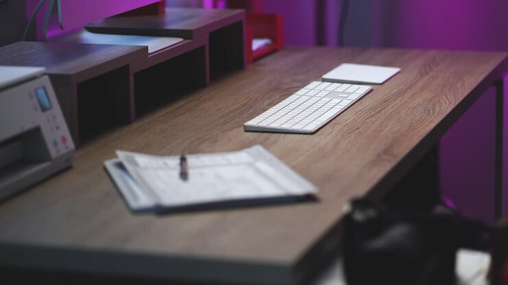 dolly shot do escritório doméstico moderno de um empresário criativo configurado com uma elegante mesa de madeira limpa, teclado de computador de alumínio branco sem fio, mouse trackpad, impressora e monitor com luz roxa