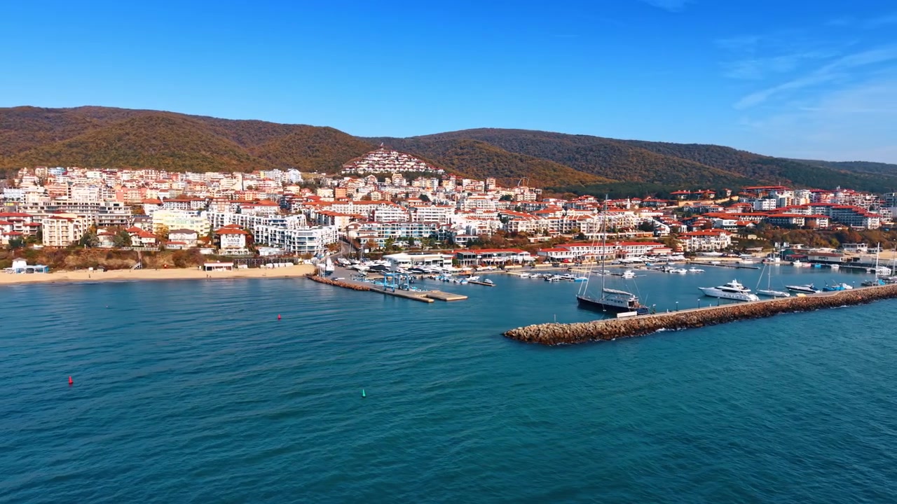 Località balneare costiera con marina e montagne, Mar Nero. Ampia vista drone di edifici bianchi, porto per yacht, spiaggia sabbiosa e acqua blu profonda.