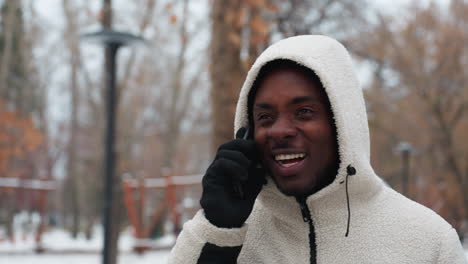 happy young man chatting on phone, chewing gum, with blurred background of trees and street light poles, showing a cheerful and lively moment in an urban outdoor setting