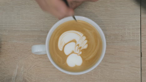 on the table is a cup of coffee with foam and the man draws on the foam pattern