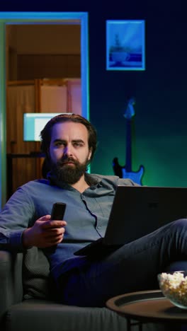 vertical video teleworker writing emails on laptop at home while watching tv