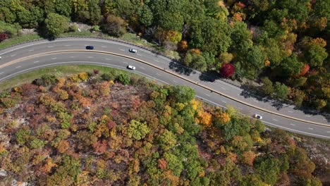 An-aerial-view-high-above-a-curved-mountain-road-in-upstate-NY-during-the-fall-foliage-changes-on-a-beautiful-day