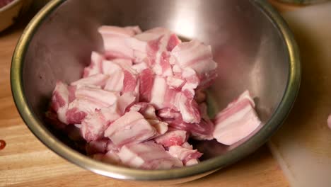 adding raw pork belly into metal mixing bowl, close up-1