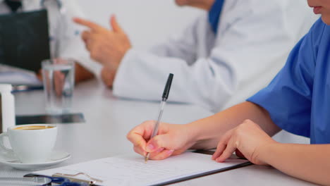 close up of nurse writing on clipboard during medical meeting