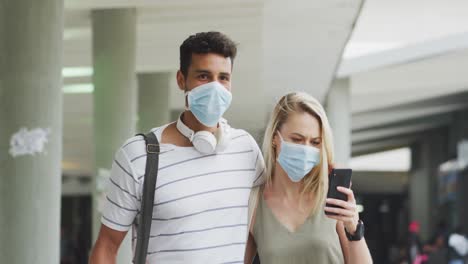 caucasian couple on the go wearing a coronavirus covid19 mask and using phone