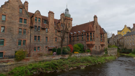 Wide-angle-slow-motion-pan-of-flowing-river-on-mossy-shores-between-brick-buildings-of-Edinburgh-Scotland