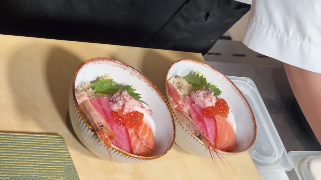 Vista dall'alto di uno chef che decora colorate ciotole di riso chirashi sushi con wasabi in un ambiente ben illuminato
