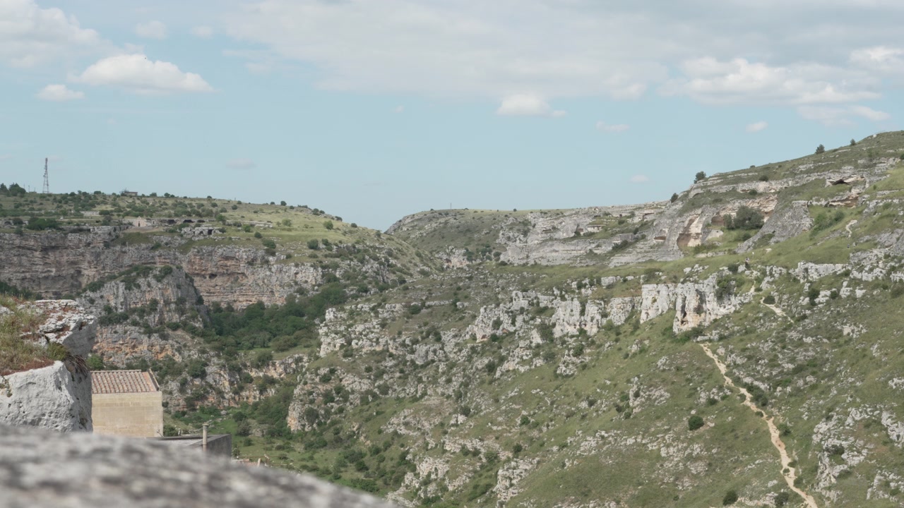 Un'ampia vista panoramica di una profonda gola rocciosa e scogliere naturali di calcare con un sentiero sterrato tortuoso per il trekking nella Provincia di Matera, Italia