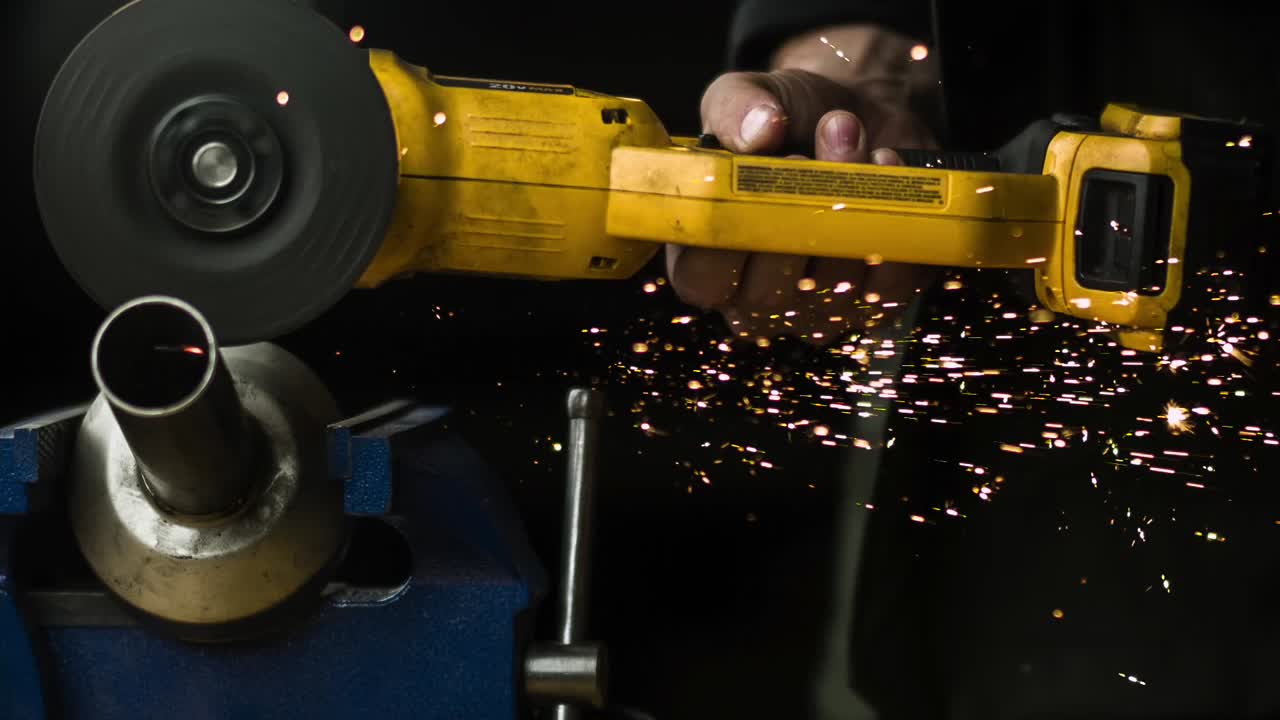 Worker's Hand Holding And Using Handheld Angle Grinder To Cut Metal On Clamp Tool. - close up, slow mo