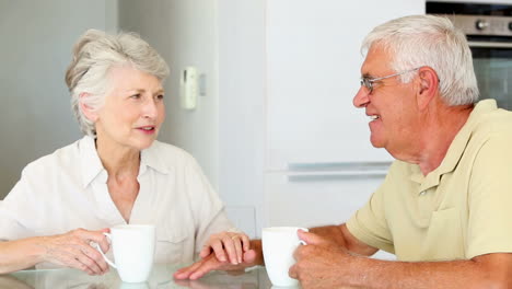 una pareja mayor sentada en la mesa tomando café.