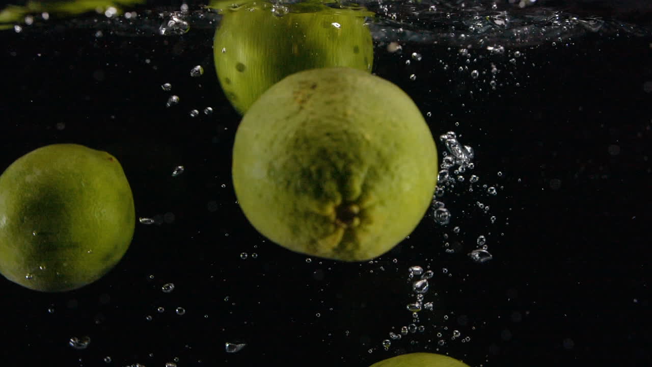 limas frescas de cítricos en cámara lenta caen en el agua con burbujas