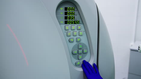 medic's hand in blue latex gloves pressing the buttons on the control panel of equipment. lab technician setting parameters on mri scanner.